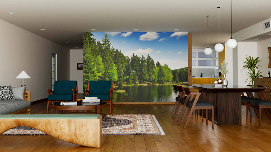 A modern open living-dining room with wood floors and mid-century furniture features the Arber Lake Germany Wall Mural as a nature-inspired focal point. Pendant lights illuminate a dark dining table with chairs.