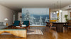 A modern living and dining area with wood floors, teal and brown furniture, and pendant lights is warmed by the Snowy Hill with Fir Trees Wall Mural, adding a wintry outdoor feel to the cozy, stylish interior.