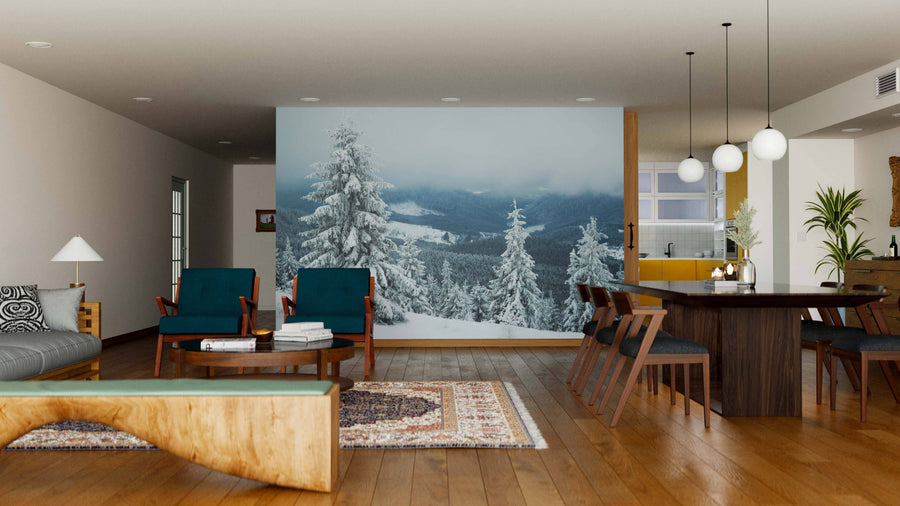 A modern living and dining area with wood floors, teal and brown furniture, and pendant lights is warmed by the Snowy Hill with Fir Trees Wall Mural, adding a wintry outdoor feel to the cozy, stylish interior.