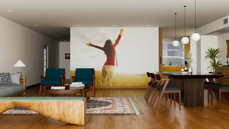 A modern living and dining area with wooden floors, mid-century furniture, pendant lights, and rugs features the Spreading Hands with Joy Wall Mural on a feature wall, separating the kitchen in the background.