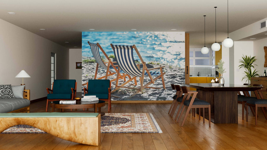 A modern living-dining room with wooden floors, stylish furniture, and the "Striped Chaise Lounges Wall Mural" depicting beach chairs on sand by water brings a coastal feel to this open-plan space.