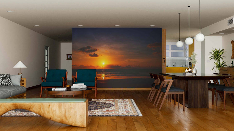 A modern living-dining room with wooden floors, teal armchairs, and a wooden coffee table features the Sun Setting on the Sea Wall Mural. Pendant lights over the dining table add to the cozy, inviting vibe.