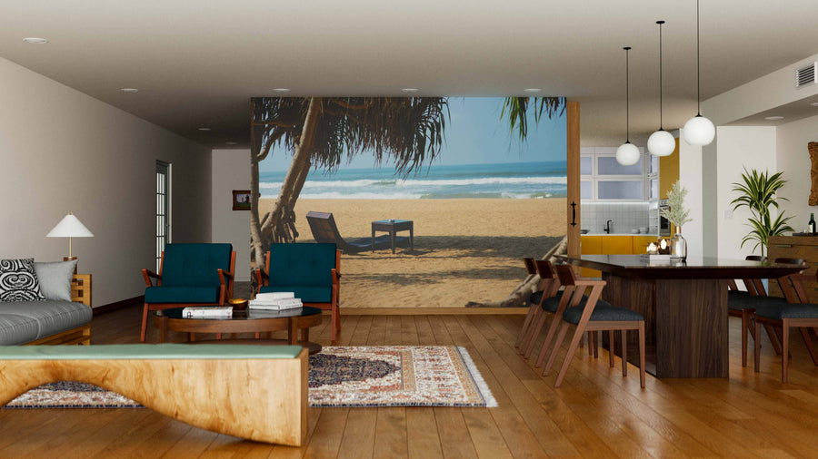 Modern living and dining room with wooden floors, teal armchairs, a large dining table, and pendant lights. The highlight is the Sunbed on Sandy Beach Wall Mural featuring sand, palm trees, and lounge chairs facing the ocean.