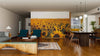 A modern living-dining room with wood floors, teal armchairs, a wooden dining table, and globe pendant lights features the Sunflower Field Wall Mural on one wall, bringing brightness to this open, stylish space.