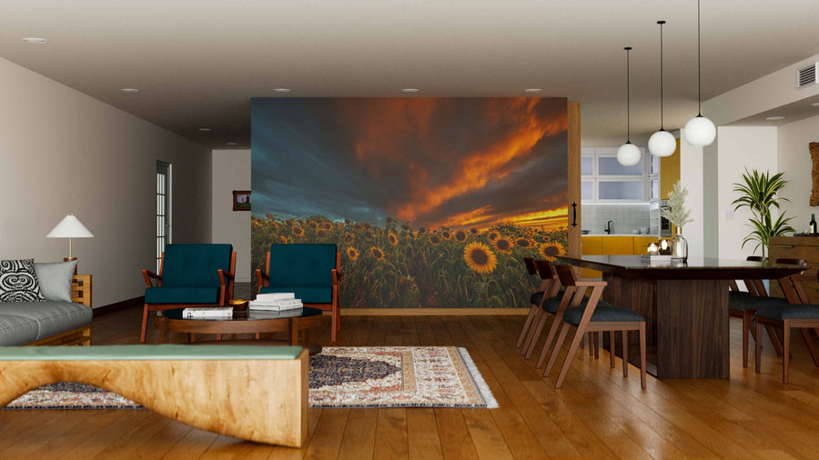 A modern open-plan living and dining room with wooden floors, mid-century furniture, and a large Sunflower Field in Bas-Rhin Wall Mural showing a dramatic sunset. Warm lighting, a rug, and the kitchen area complete this inviting space.