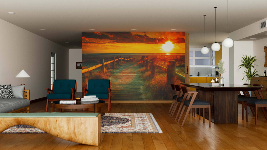 A modern living-dining area with wood floors and blue armchairs features the Sunset Beach Wall Mural, a peel and stick removable wallpaper with a dramatic boardwalk sunset, adding golden light and style that's easy to refresh.