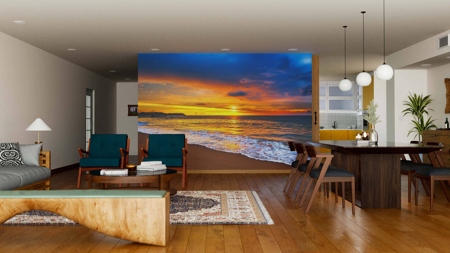 A modern open-concept living and dining area, with wooden floors and mid-century furniture, features the "Sunset Over the Blue Sea Wall Mural," adding vibrant blues, oranges, and yellows of a beach sunset with waves to the space.