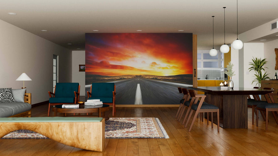 A modern living and dining room with wooden floors, mid-century furniture, and the Sunset Strip Wall Mural—a large peel and stick mural featuring a dramatic, colorful sunset over a road—creates a striking focal point in the open, warmly lit space.