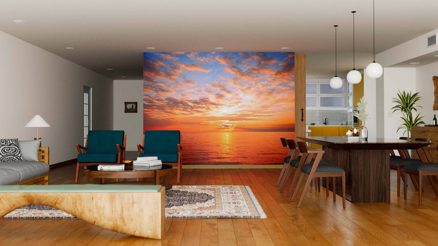 A modern living-dining room with wooden floors, teal chairs, a wooden table, pendant lights, and the "Sunset at the Sea Wall Mural," featuring a vibrant orange sunset over the ocean for a warm, inviting touch.