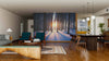 A modern living-dining room features wood floors, mid-century furniture, and the "Sunset in the Woods in Winter Wall Mural," bringing natural warmth and sunlight to the stylish interior with its snowy forest scene.