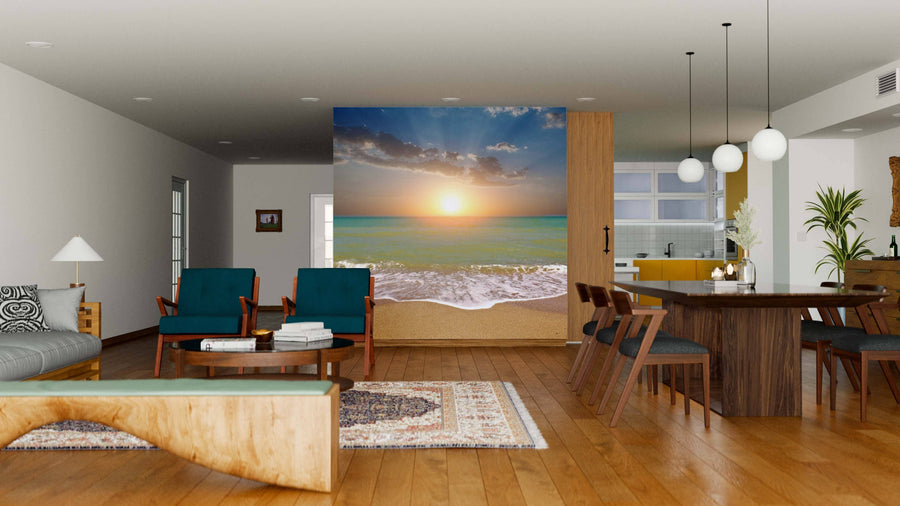 A modern open-concept living and dining room with wood floors, teal chairs, a wooden table, and the Sunset on Green Sea Wall Mural brings vibrant beach vibes indoors with ocean waves and a bright sky.