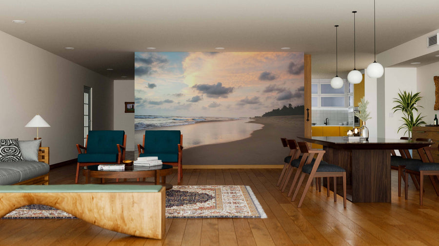 A modern living and dining room with wooden floors features teal chairs, a wooden table, pendant lights, and the "Sunset over Tropical Beach Wall Mural." The open space is warmed by a rug and minimalist decor.