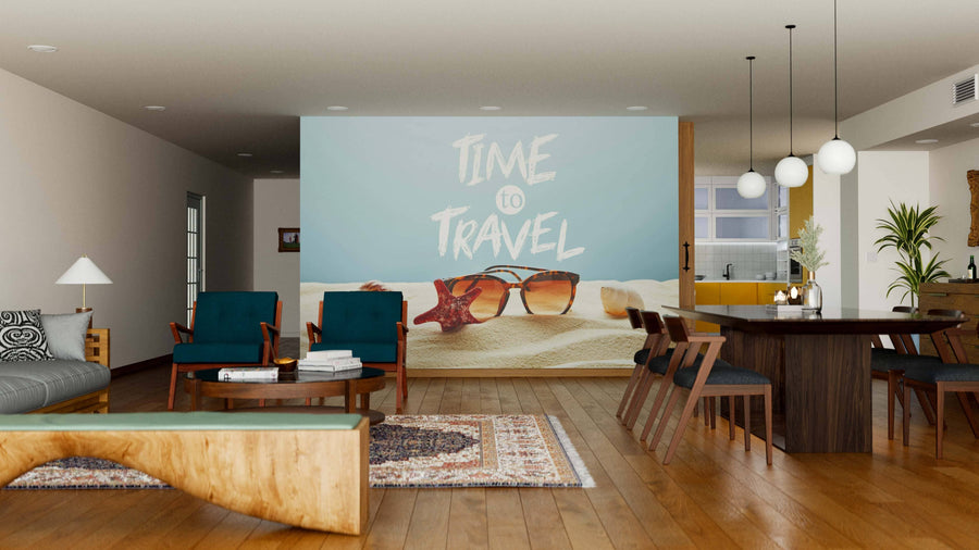 A modern living-dining area with wood floors, blue armchairs, and a dining set is brightened by the Time to Travel Wall Mural, featuring sunglasses and sand for a beachy, vacation vibe.
