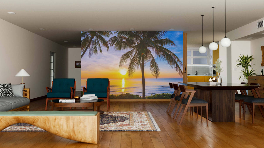 A modern living and dining room with wooden floors, rugs, green armchairs, a dining table, and pendant lights features a Tropical Landscape Wall Mural of palm trees at sunset over the ocean for a tropical vibe.