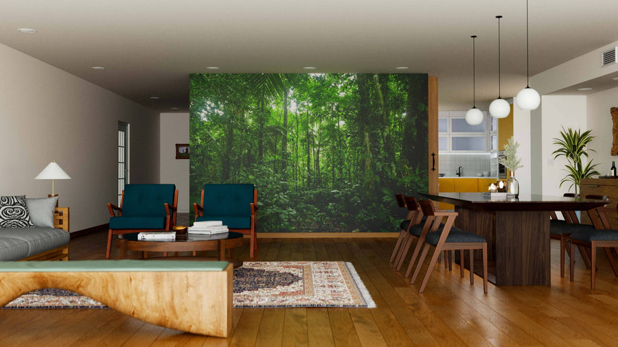 A modern open-plan living and dining room with wooden floors, teal armchairs, and a dark dining table features the Tropical Rainforest Landscape Wall Mural as a lush focal point. Pendant lights hang above the table; large windows bring in natural light.