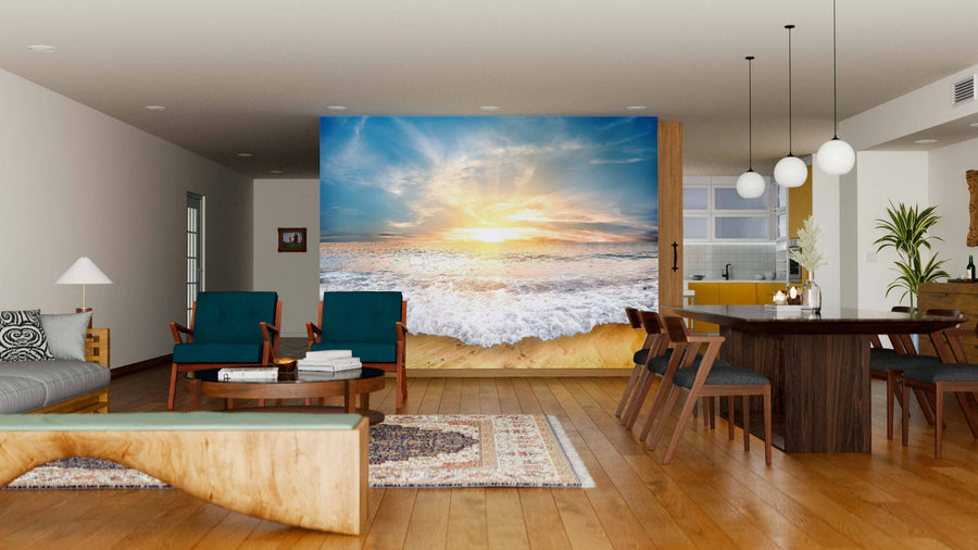 A modern living-dining room with wood floors, green armchairs, a sofa, and a large Unreal Beach Wall Mural. Sunlight from the window by the kitchen highlights the dining table and globe pendant lights.