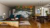 A modern living-dining area features wood floors, teal armchairs, and a dining set. The Upper Bond Falls Wall Mural depicting an autumn forest waterfall adds vibrance, while pendant lights hang above the table.