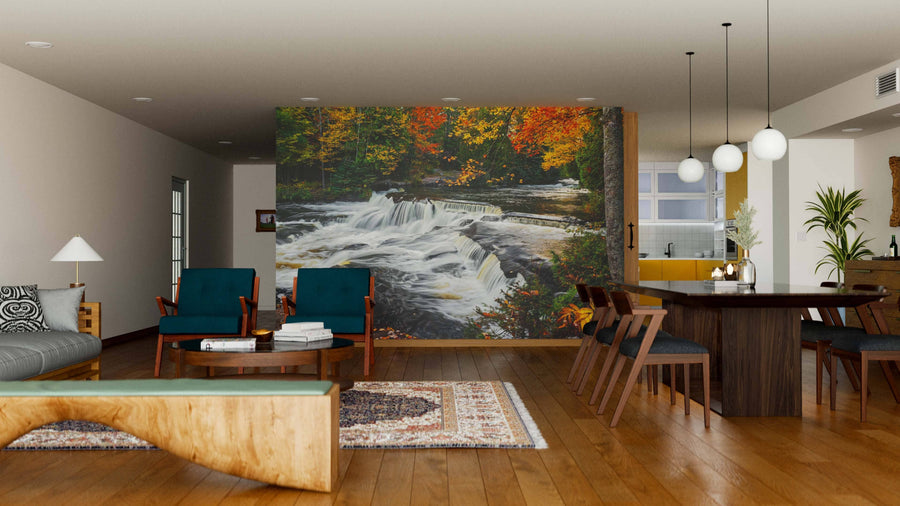 A modern living-dining area features wood floors, teal armchairs, and a dining set. The Upper Bond Falls Wall Mural depicting an autumn forest waterfall adds vibrance, while pendant lights hang above the table.