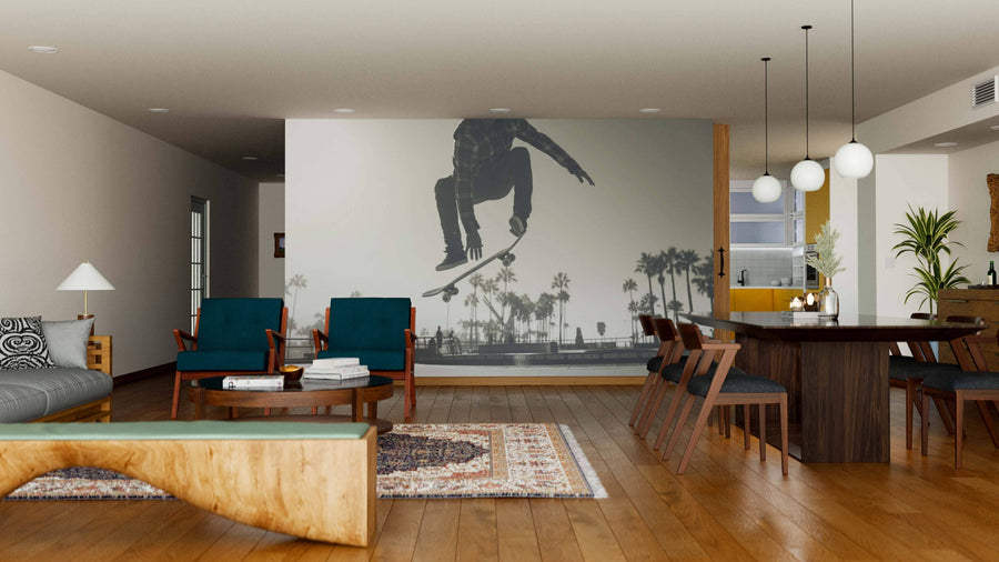Spacious modern living and dining room with wooden floors, mid-century furniture, a large Venice Wall Mural featuring a skateboarder above palm trees, a rug, blue chairs, wooden table, pendant lights, and neutral walls.