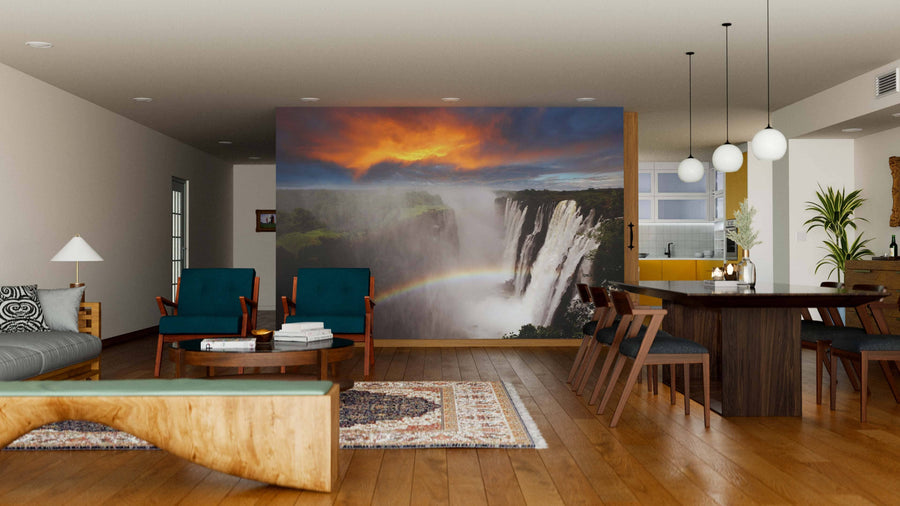Modern open-plan living and dining area with wooden furniture and neutral walls, featuring the Victoria Falls with Rainbow Wall Mural under a fiery sunset sky as a dramatic focal point.