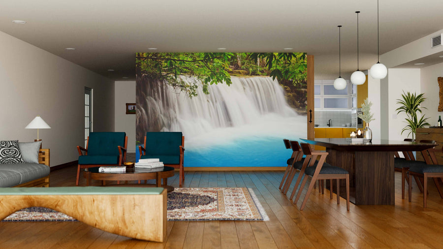 A modern living and dining room features wooden floors, teal chairs, a large dining table, and the Waterfalls Kanchanaburi Thailand Wall Mural. Pendant lights hang above the table, and natural light fills the inviting space.
