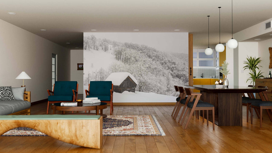 A modern, open living-dining space features wood floors, teal armchairs, a gray sofa, a wooden dining table under pendant lights, and a Winter Landscape with Wooden House Wall Mural that adds striking visual interest to one wall.