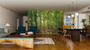 A modern living-dining room features wood flooring, mid-century furniture, a Wisconsin Green Forest Wall Mural on one wall, and globe pendant lights above a dark dining table. Natural light fills this cozy, nature-inspired space.
