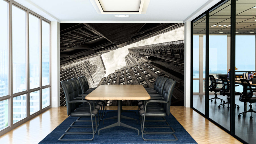A modern conference room features a long wooden table, black chairs, glass walls, and the striking "Lonely Towers Wall Mural" depicting tall city skyscrapers. Floor-to-ceiling windows fill the space with light; another office is visible through the glass.