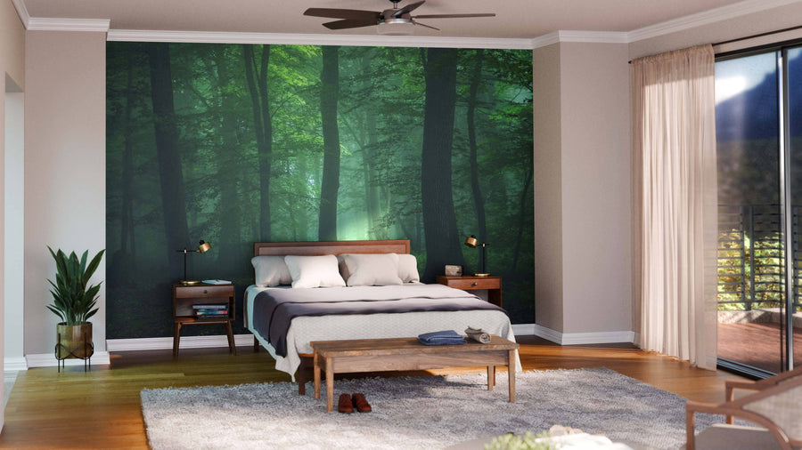 A modern bedroom features the Lost in a Foggy Forest Wall Mural, a wooden bed with white and gray bedding, matching nightstands with lamps, a wooden bench, gray rug, plant, and glass doors with sheer curtains letting in natural light.