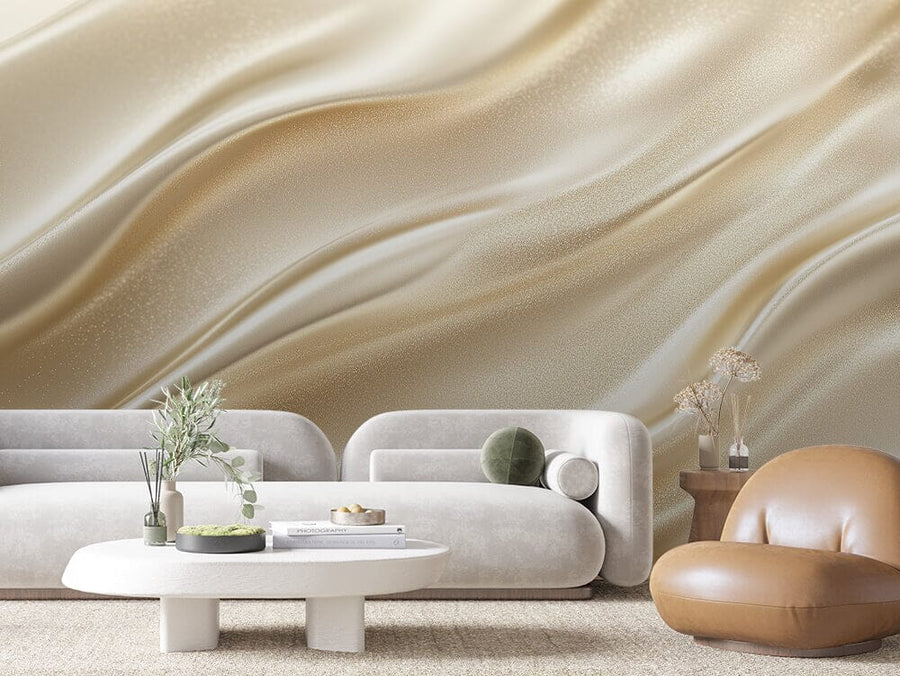 A modern living room features the Luminous Silk Wall Mural in beige and cream waves, paired with two white sofas, a round coffee table with books and a plant, a tan leather chair, and a side table holding dried flowers, embodying minimalist elegance in neutral tones.