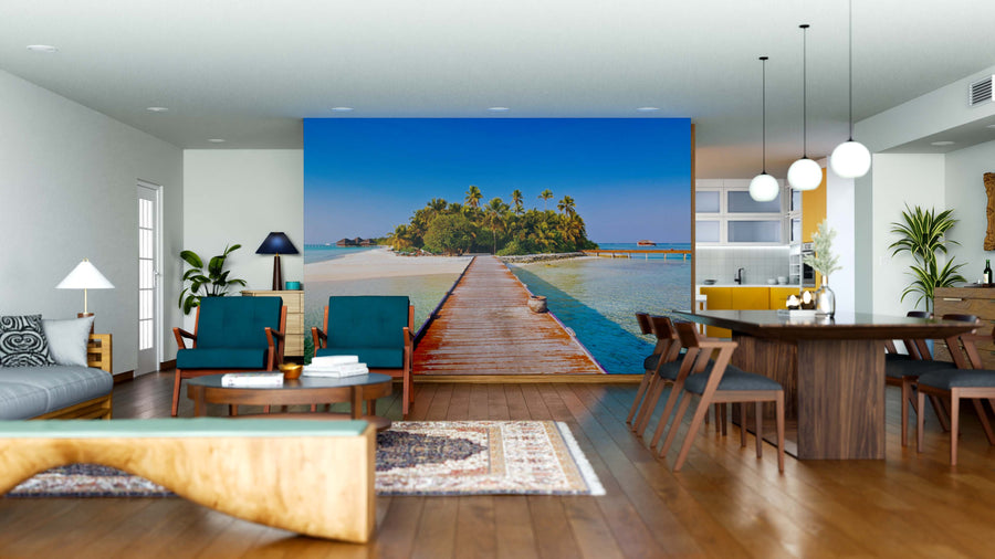 A modern living-dining room with wooden furniture and pastel accents is enhanced by the Maldives Wall Mural—a large peel-and-stick mural depicting a tropical island, wooden pier, clear blue sky, and turquoise water for vibrant, exotic depth.