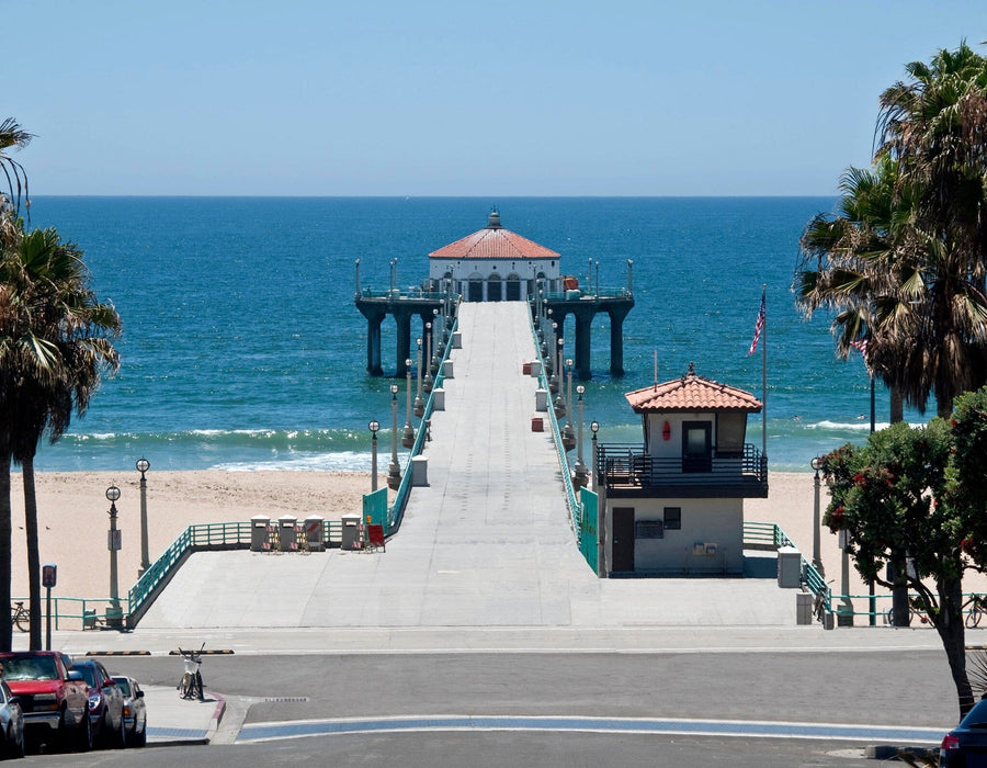 A modern living and dining room with wood floors and mid-century furniture features the Manhattan Beach Pier Wall Mural, a peel-and-stick decor option that frames a stunning ocean view for easy, stylish ambiance.