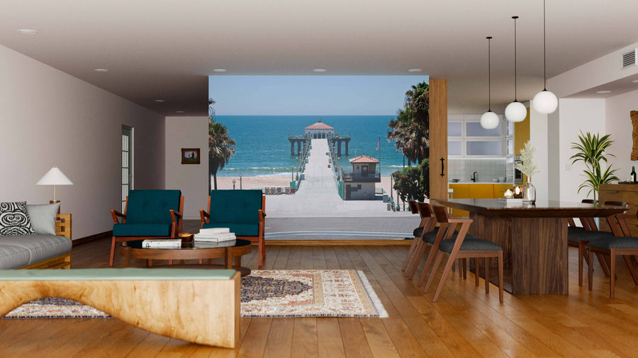 A modern living and dining room with wood floors and mid-century furniture features the Manhattan Beach Pier Wall Mural, a peel-and-stick decor option that frames a stunning ocean view for easy, stylish ambiance.