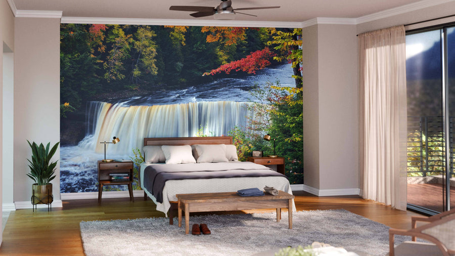 A modern bedroom showcases the Michigan's Tahquamenon Falls Wall Mural behind the bed, with neutral walls, wooden furniture, a ceiling fan, potted plants, gentle lighting, and large windows with sheer curtains allowing in natural light.