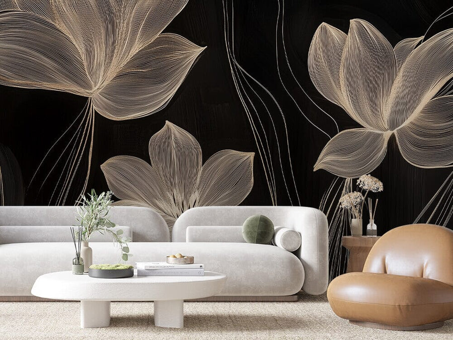 A modern living room features the Midnight Blooms Wall Mural with black floral wallpaper and beige line-art flowers. It includes two white, rounded sofas, a brown leather chair, and a white oval coffee table with a plant and book. The light carpet beautifully complements the neutral tones.