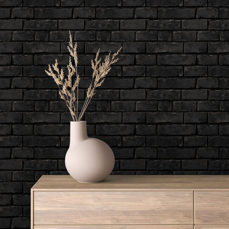 A minimalist scene features a round beige vase with tall dried grass on a light wooden dresser. The Midnight Brickwork Wall Mural's dark, textured design contrasts with the vase and dresser, highlighting simplicity and modern style.