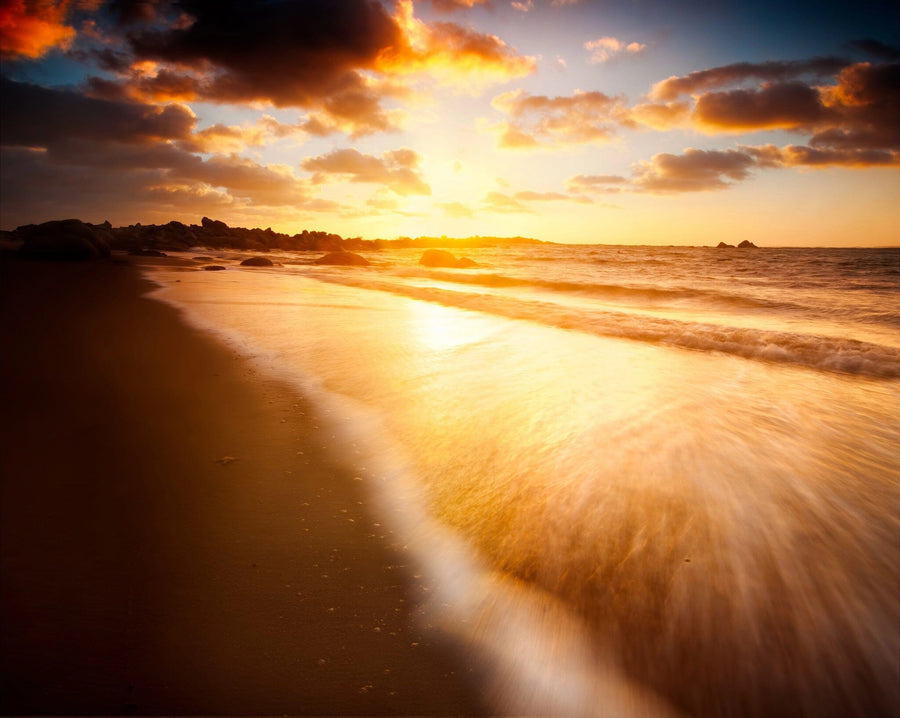 Transform your space with the Australian Beach Wall Mural, featuring a serene sunset with orange, yellow, and blue hues. Gentle waves reflect warm sunlight onto a sandy shore while distant rocks enhance the tranquil horizon in this breathtaking peel-and-stick wall mural.