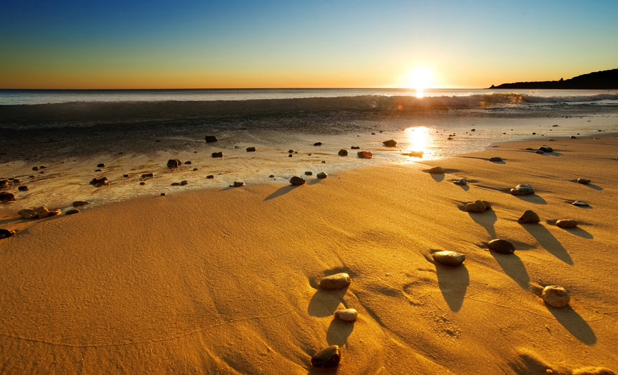 A serene beach sunset with rocks scattered on the sand