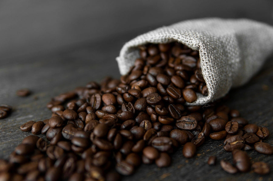 The Burlap Bag of Beans Wall Mural features dark roasted coffee beans spilling from a burlap sack onto rustic wood, creating rich texture and warmth for any space with easy-to-install, removable wallpaper.