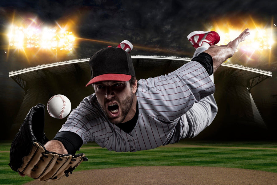 The Catching Baseball Wall Mural shows a player in a gray pinstripe uniform and black cap diving on a night field, arm outstretched with glove to catch the ball. Bright stadium lights illuminate the dramatic canvas-textured scene.
