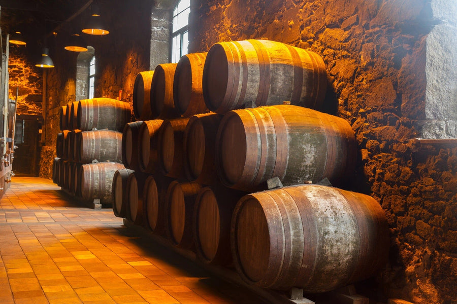 A dimly lit cellar with rows of stacked wooden barrels against a stone wall, enhanced by the Cellar Barrel Stacks Wall Mural from for added charm. Warm light from hanging lamps creates a cozy atmosphere, illuminating the aged textures and tiled floors for a rustic vibe.