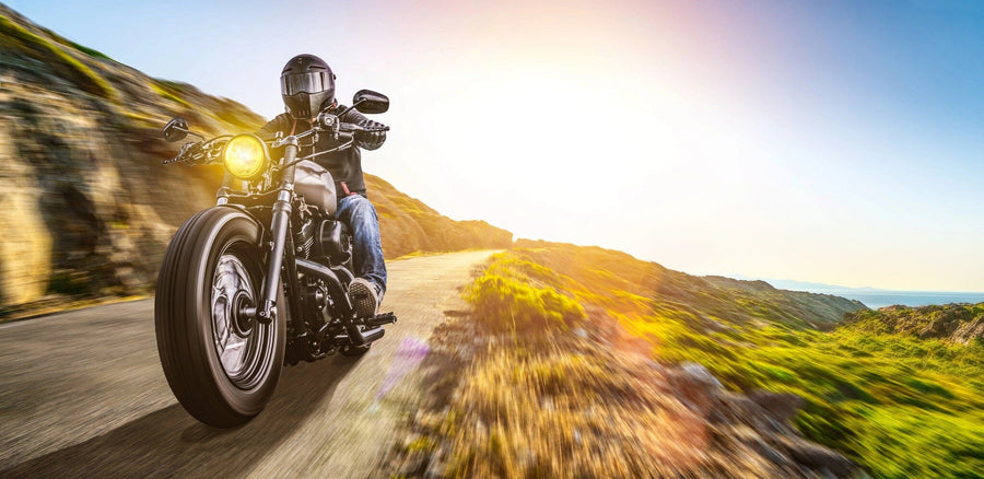 In the "Motor 26 Wall Mural," a motorcyclist in a black helmet rides a cruiser bike on a winding road, framed by rocky hills and lush greenery at sunset. The warm glow casts over the scene as the headlight brightens the path ahead, capturing the essence of adventure.