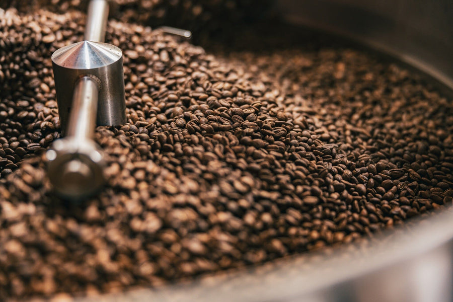 The Coffee Roast Wall Mural features a close-up of freshly roasted coffee beans in a metal roasting machine, with shiny rods and rich brown tones—ideal for custom printed murals or removable wallpaper, evoking the aroma and warmth of fresh coffee.