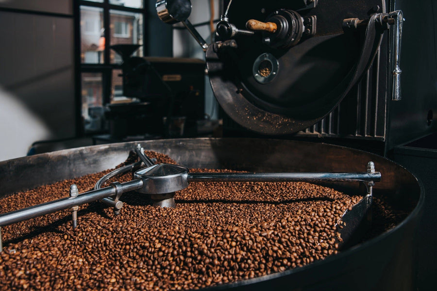 Close-up of the Coffee Roasting Process Wall Mural featuring a coffee roasting machine with rich brown roasted beans inside. Shiny metal arms stir the beans, while sunlight through a window illuminates the scene—ideal for custom printed murals.