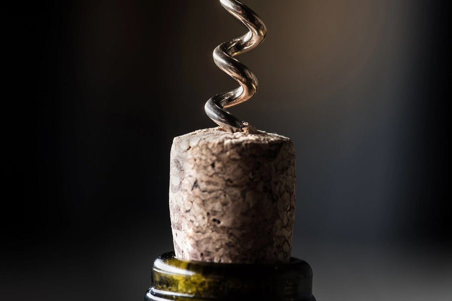 A close-up of the cork partially removed from a wine bottle by a metal corkscrew resembles an intricate scene from the Wine 18 Wall Mural. The natural cork contrasts with the dark green bottle lip, and a dark background enhances this dynamic focus moment.