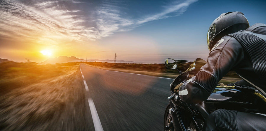 A motorcyclist in black gear speeds down a road at sunset, evoking the dynamic imagery of the Endless Open Road Wall Mural. The blurred background heightens the speed effect, while the warm landscape glow echoes custom printed murals.