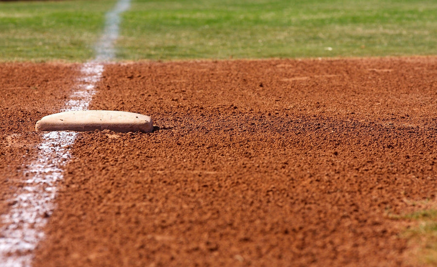 Bright and vibrant, the First Base Wall Mural features a close-up of first base on reddish-brown dirt with a white chalk foul line and green grass—a sunlit scene perfect for personalized decor in peel-and-stick format.