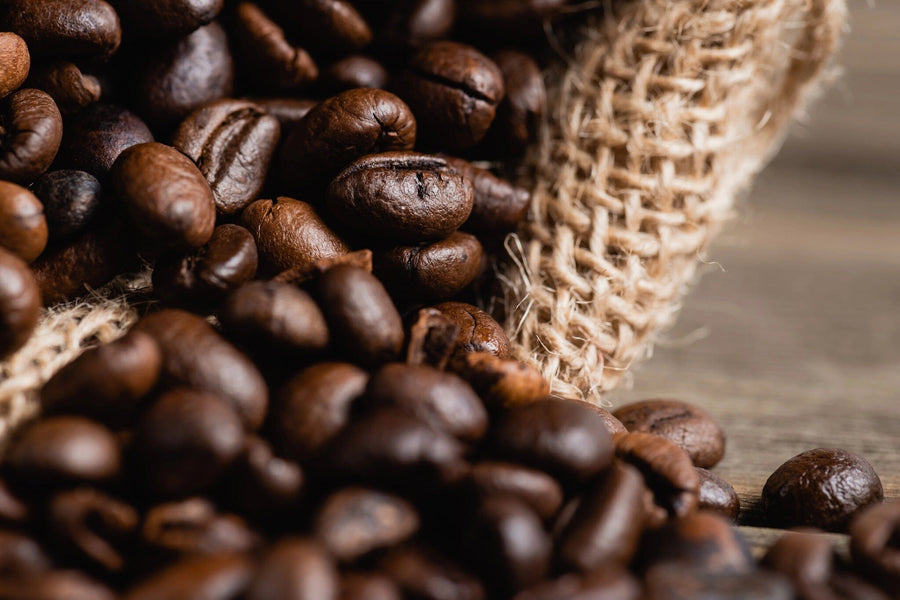 Close-up of roasted coffee beans spilling from a sack onto wood, captured in detail for the Fresh Coffee Roast Wall Mural. The rich textures make this image perfect for peel and stick wall murals or removable wallpaper.