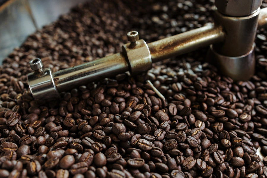 Close-up of roasted coffee beans in a metal roasting machine with glossy beans and a rotating arm—ideal inspiration for the Fresh Roast Wall Mural, perfect for celebrating artisanal coffee moments on your walls.