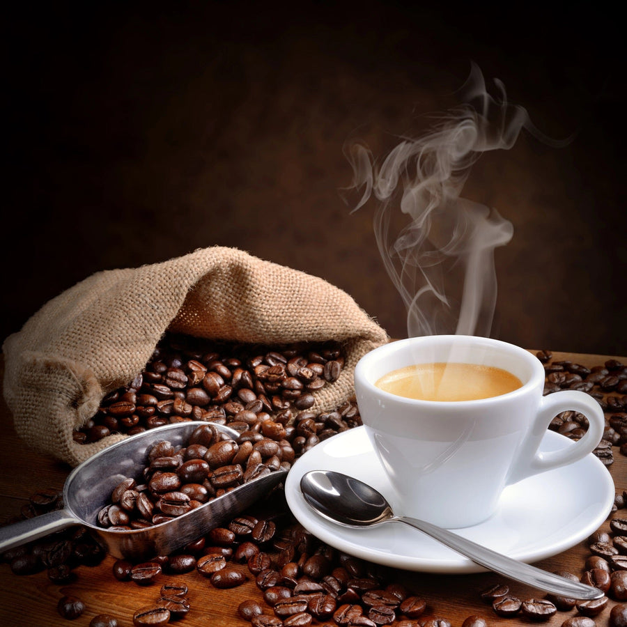 A steaming cup of coffee on a saucer with a spoon sits amid spilled beans—a cozy scene featured in the Coffee 6 Wall Mural, perfect as a custom print or peel and stick mural to warm up your space.
